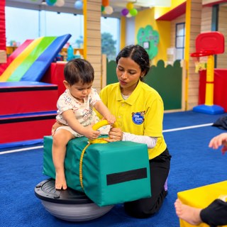 Coach helping a baby balance on a padded block at My Gym Ludhiana